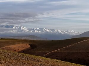 Paesaggio del deserto africano con colline aride in primo piano e le montagne innevate dell'Atlante sullo sfondo